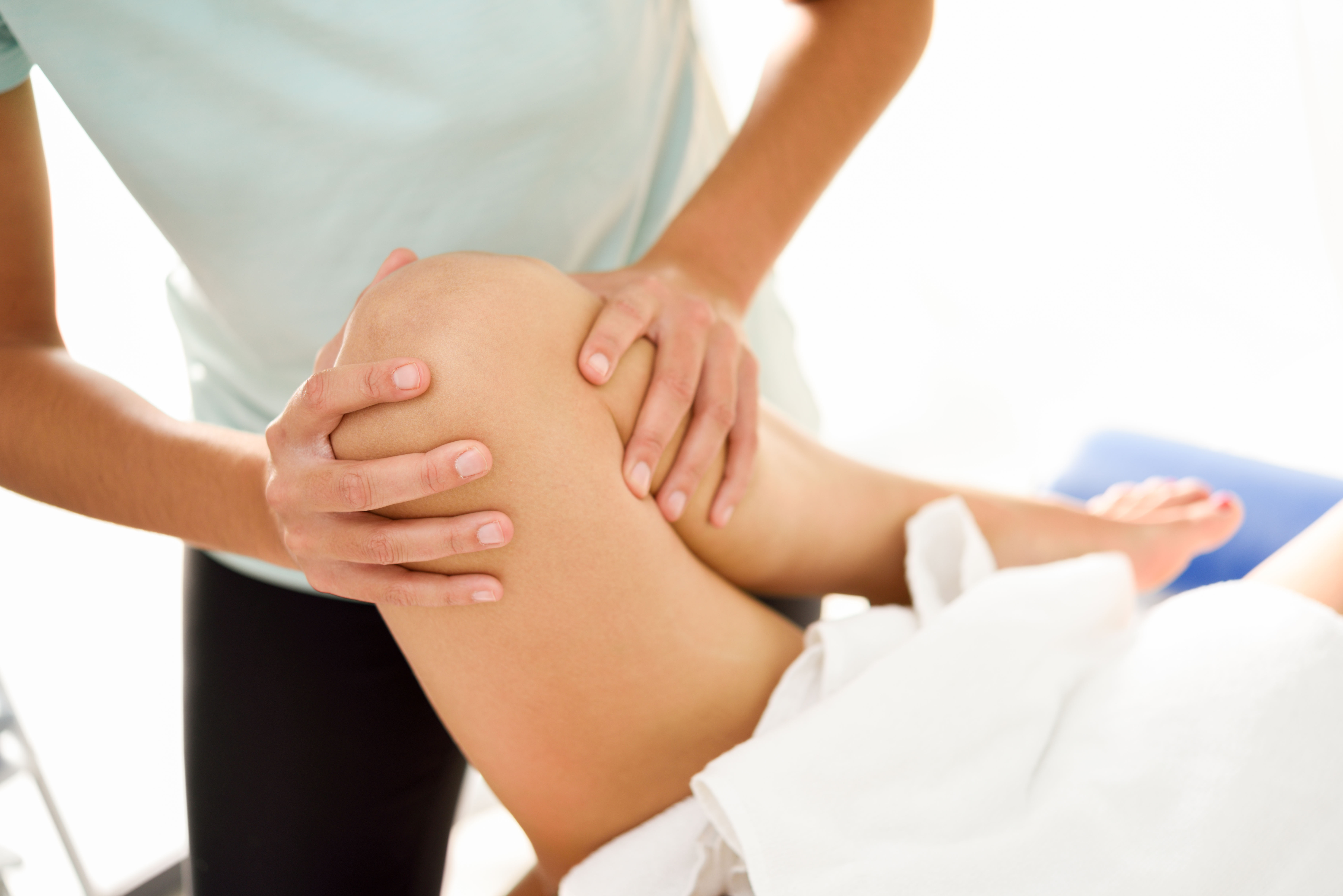 Medical massage at the leg in a physiotherapy center. Female physiotherapist inspecting her patient. Close-up photograph.